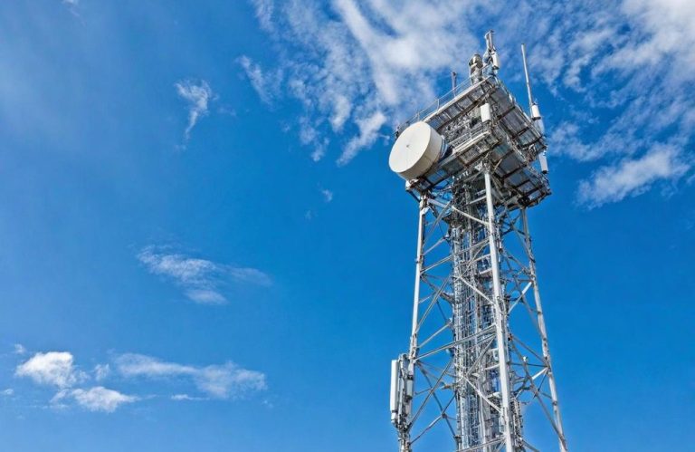 Unter einem klaren blauen Himmel steht ein großer Mobilfunkmast aus Metall.